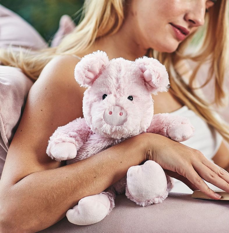 A pink plush toy pig that is fully heatable and can be microwaved to provide warmth.