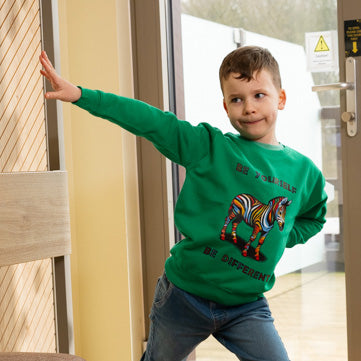 A boy wearing a green sweatshirt with a rainbow-colored zebra and the text 'BE YOURSELF BE DIFFERENT' on it.