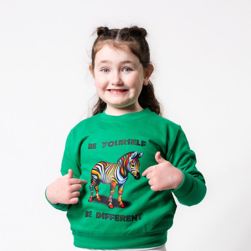 A child wearing a green sweatshirt with a rainbow-colored zebra and the text 'BE YOURSELF BE DIFFERENT' on it.