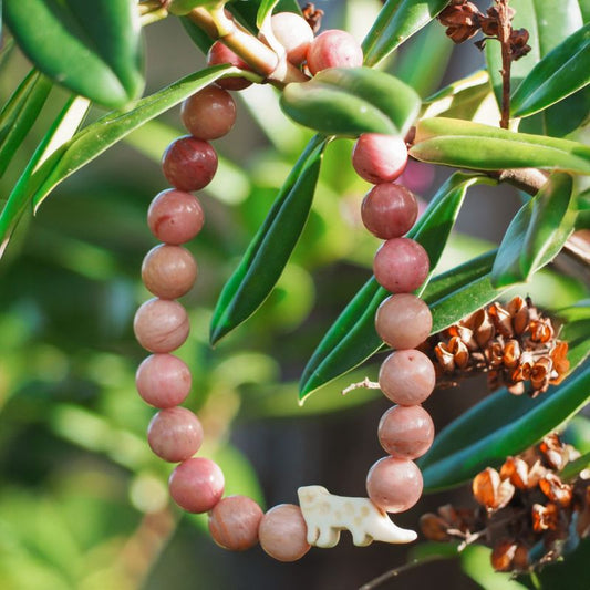 Beaded fahlo bracelet with pink beads and a white snow leopard charm on a green leafy background