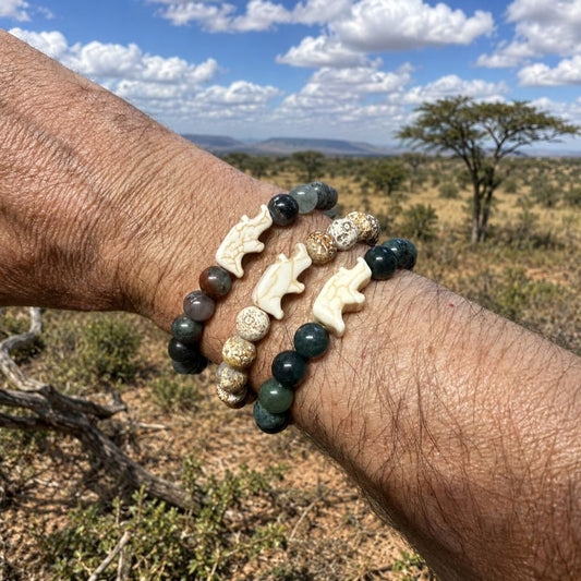 Bracelet with beads with a rhino charm on a wrist against a natural landscape.