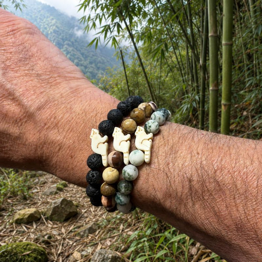 Arm wearing several beaded bracelets with red panda charms against a himalayan forest background