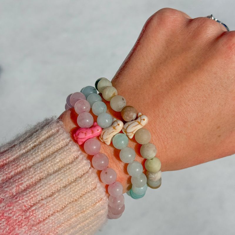 Arm wearing multiple beaded fahlo bracelets with penguin charms on a plain background
