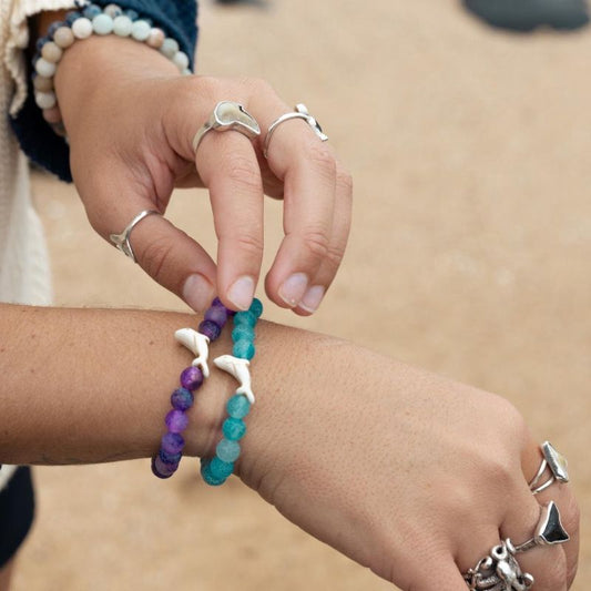 Close-up of arms wearing beaded bracelets with dolphin charms on a beach background