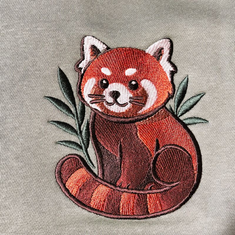Embroidered red panda patch on a green fabric background