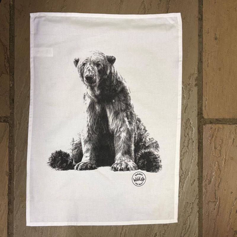 A white tea towel featuring a detailed black and white sketch of a polar bear, displayed flat against a rustic brown flagstone background.
