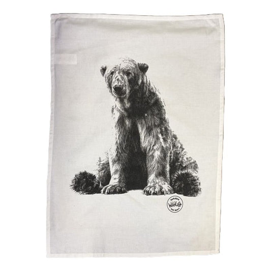 A rectangularwhite tea towel featuring a detailed black and white sketch of a bear sitting down, with a small circular yorshire wildlife park logo printed near the bottom right.