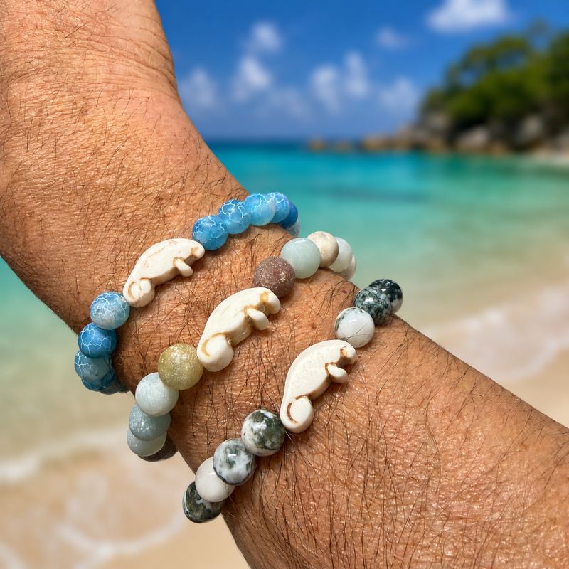 Beaded bracelets with manatee charms on a wrist against a beach background