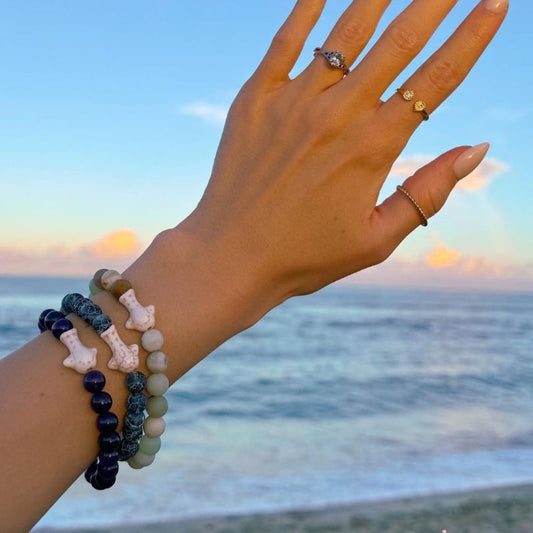 Arm wearing multiple beaded bracelets with whale shark charms with a sunset over water background