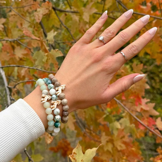 Arm with multiple beaded fahlo bracelets and wolf charms and an autumn leaf background