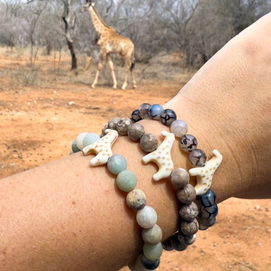 Fahlo bracelet with giraffe charms on a wrist in front of a giraffe in a natural setting